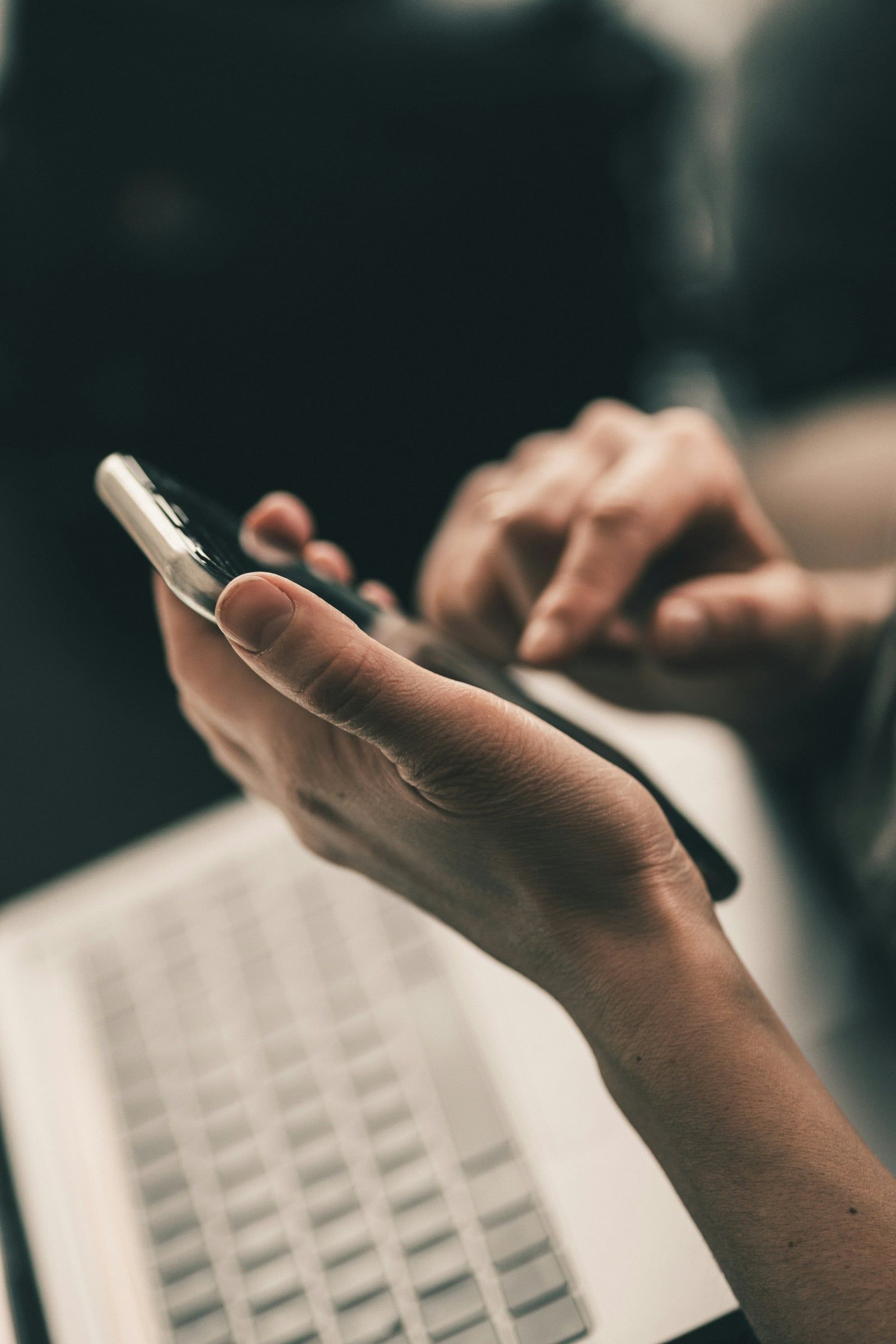 Hands using a smartphone above a laptop keyboard
