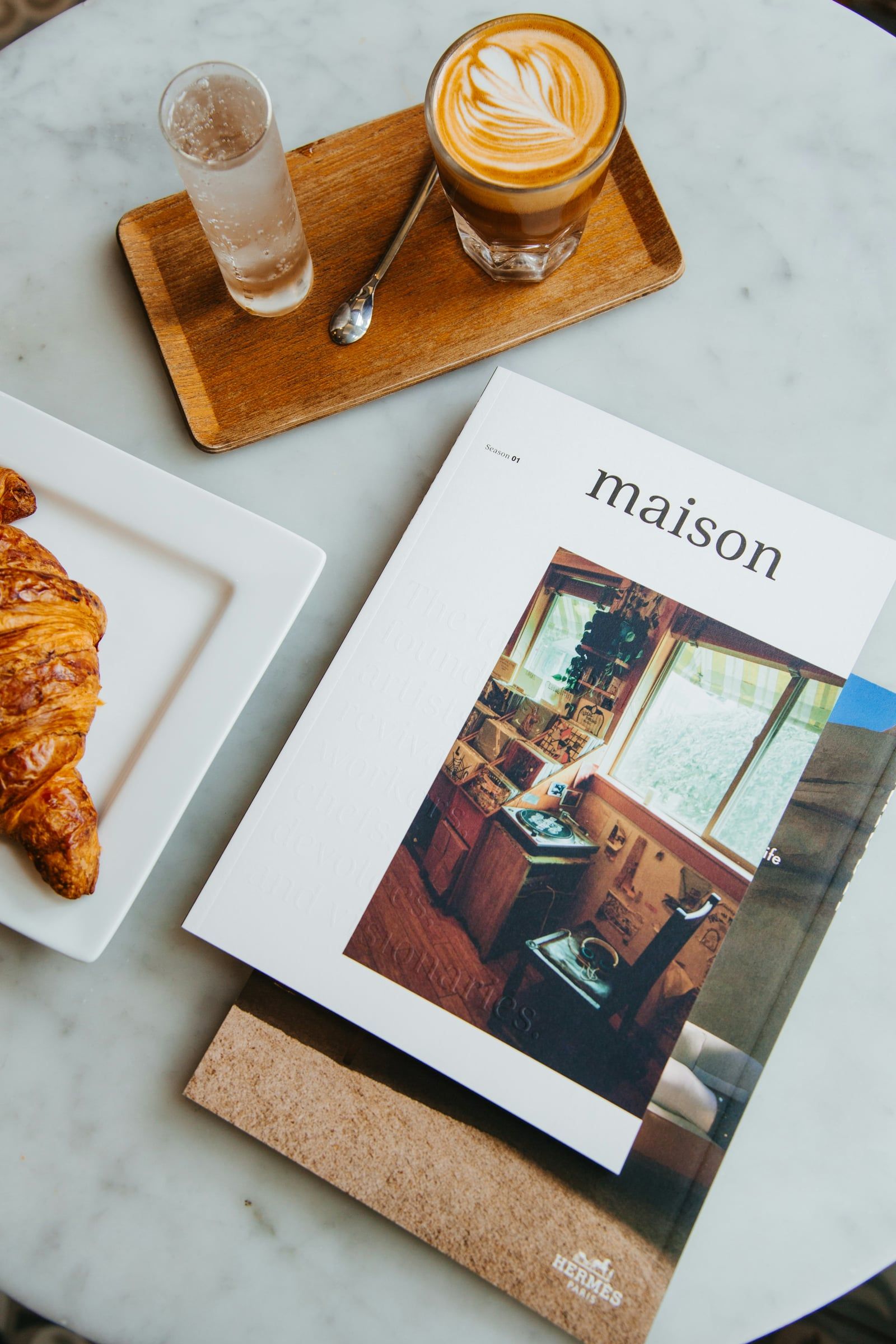 Printed magazine beside a coffee and croissant on a marble table