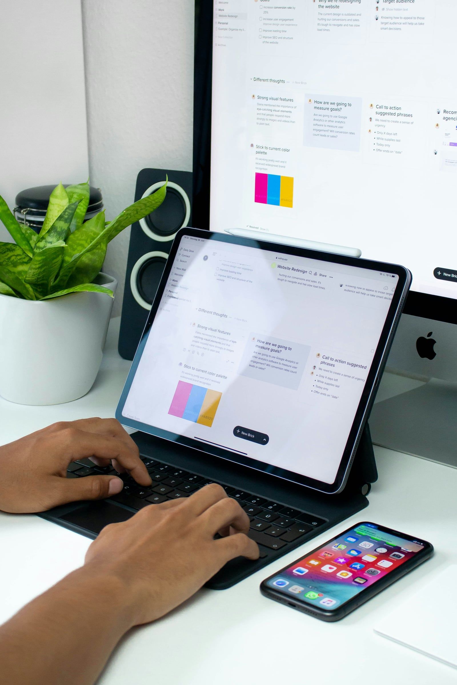 Hands typing on a tablet keyboard in front of a monitor showing a website redesign plan